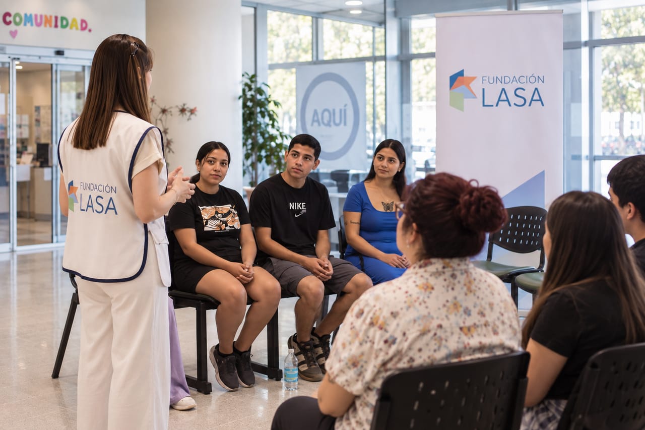 Una facilitadora de Fundación LASA, con su chaleco institucional, guía una conversación con un grupo sentado en círculo en un hall amplio y luminoso